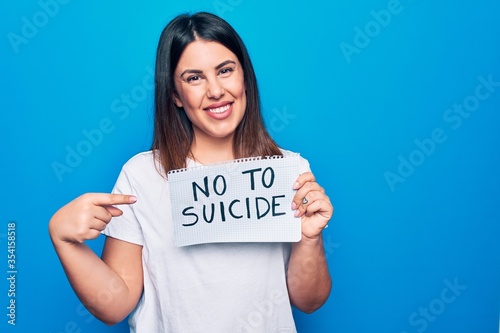 Young beautiful woman asking for psychical problem holding paper with not to suicide message smiling happy pointing with hand and finger photo