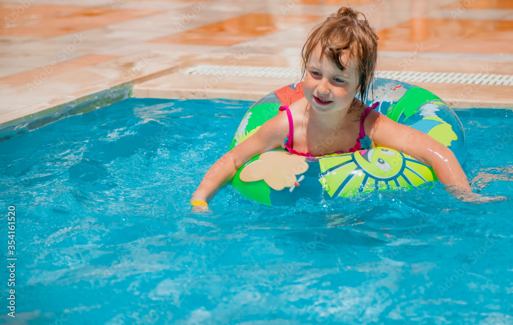 Poprtrait of little cute child girl swimming with colorful ring outdoors in pool. Summer holiday and happy childhood concept.