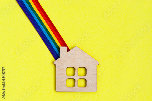 mini toy wooden house and lgbt rainbow ribbbon on yellow background photo