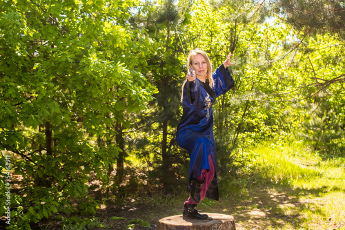 Fototapeta Naklejka Na Ścianę i Meble -  A woman in a blue kimono poses with a sword in the forest standing on a stump