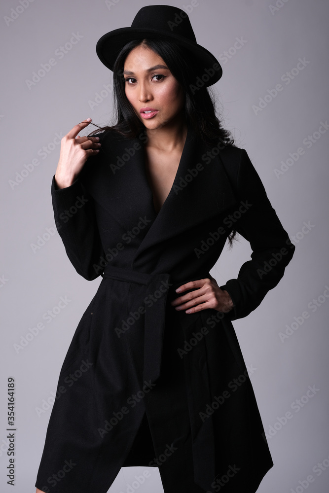 Elegant and chic asian model in black coat and hat. Studio shoot. Elegant and chic asian model in black coat and hat. Studio shoot.