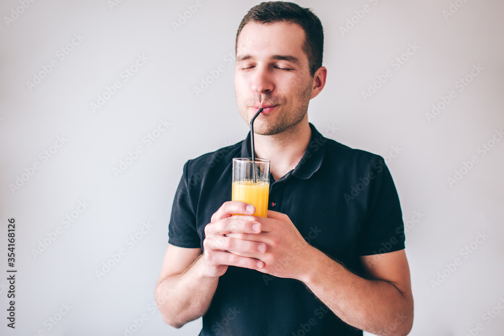 Young man isolated over background. Delightful happy guy drinking orange juice through plastic straw. Hold glass in hands. Positive cheerful man. Young man isolated over background. Delightful happy guy drinking orange juice through plastic straw. Hold glass in hands. Positive cheerful man.