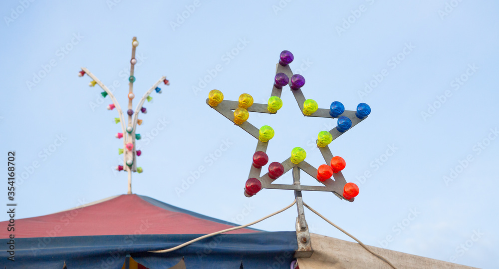 Carousel roof with multicolored illumination at top of that. Selective focus on star-shaped lamp with colorful light bulbs in foreground. Illumination backlight concept. Carousel roof with multicolored illumination at top of that. Selective focus on star-shaped lamp with colorful light bulbs in foreground. Illumination backlight concept.