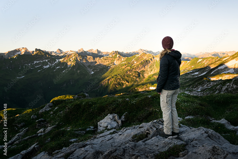 Young woman is looking at Allgäu Mountains near Oberstdorf in the german Alps during sunrise on a clear refreshing morning