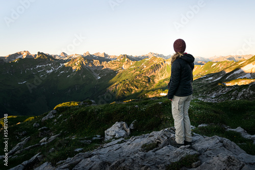 Young woman is looking at Allgäu Mountains near Oberstdorf in the german Alps during sunrise on a clear refreshing morning