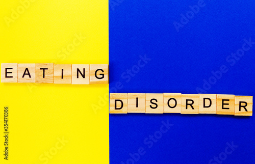 words eating disorder. Wooden blocks with an inscription on top on a yellow and blue background. Social problems of teenagers