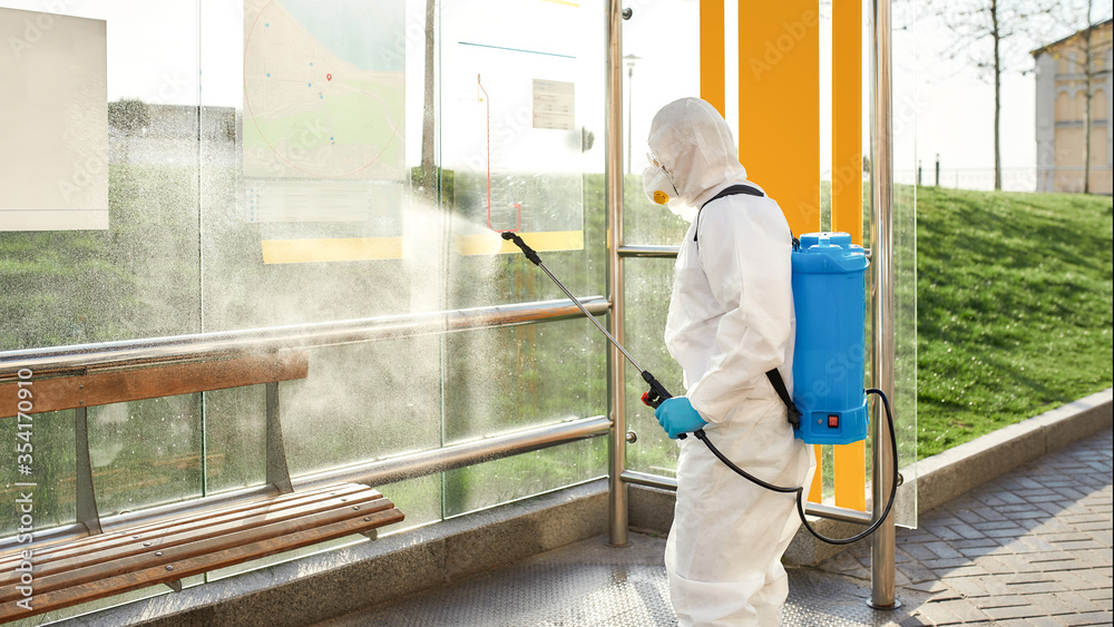 No germs allowed. Sanitization, cleaning and disinfection of the city due to the emergence of the Covid19 virus. Man in protective suit and mask at work near the bus stop