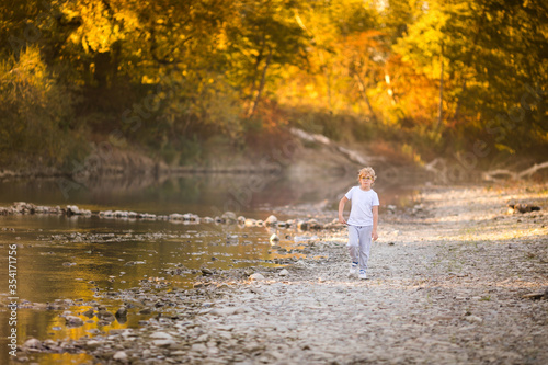 Little blonde boy in green glasses playing on the riverside. Autumn in the yellow forest