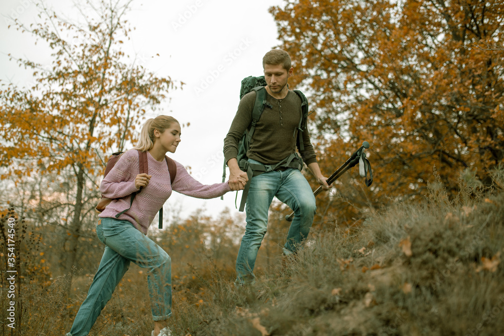 Loving couple of tourists climb the slope holding hands. Cheerful Young Couple, man and a woman with backpacks travel together in autumn nature. Hiking concept. Healthy lifestyle concept. Loving couple of tourists climb the slope holding hands. Cheerful Young Couple, man and a woman with backpacks travel together in autumn nature. Hiking concept. Healthy lifestyle concept.