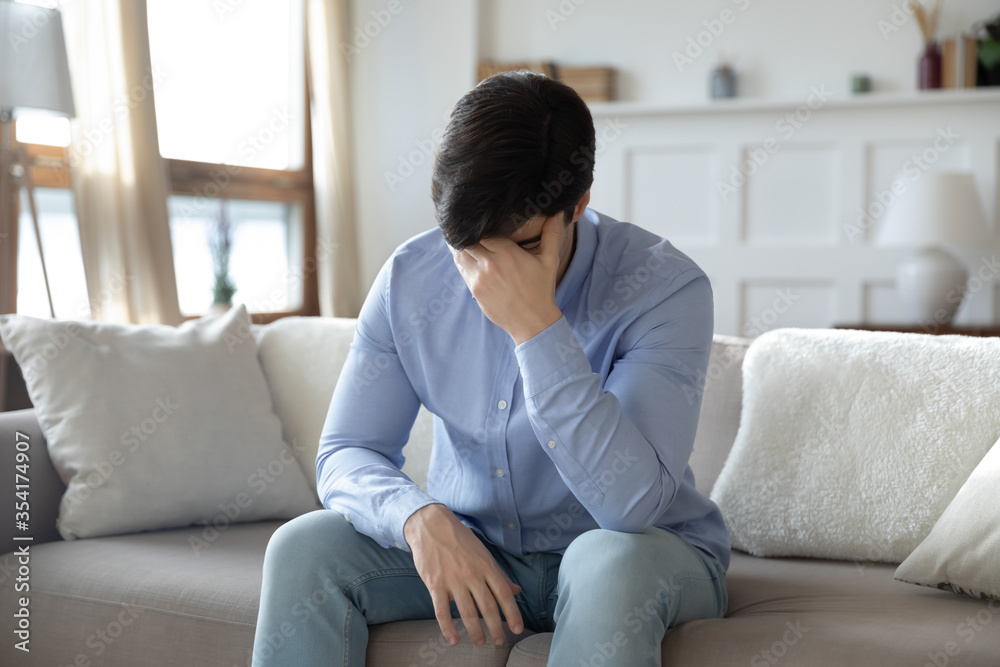 Upset young caucasian man sit on sofa in living room feeling depressed distressed with life relationships problems, unhappy sad millennial male suffer from mental or psychological issue, yearn at home Upset young caucasian man sit on sofa in living room feeling depressed distressed with life relationships problems, unhappy sad millennial male suffer from mental or psychological issue, yearn at home
