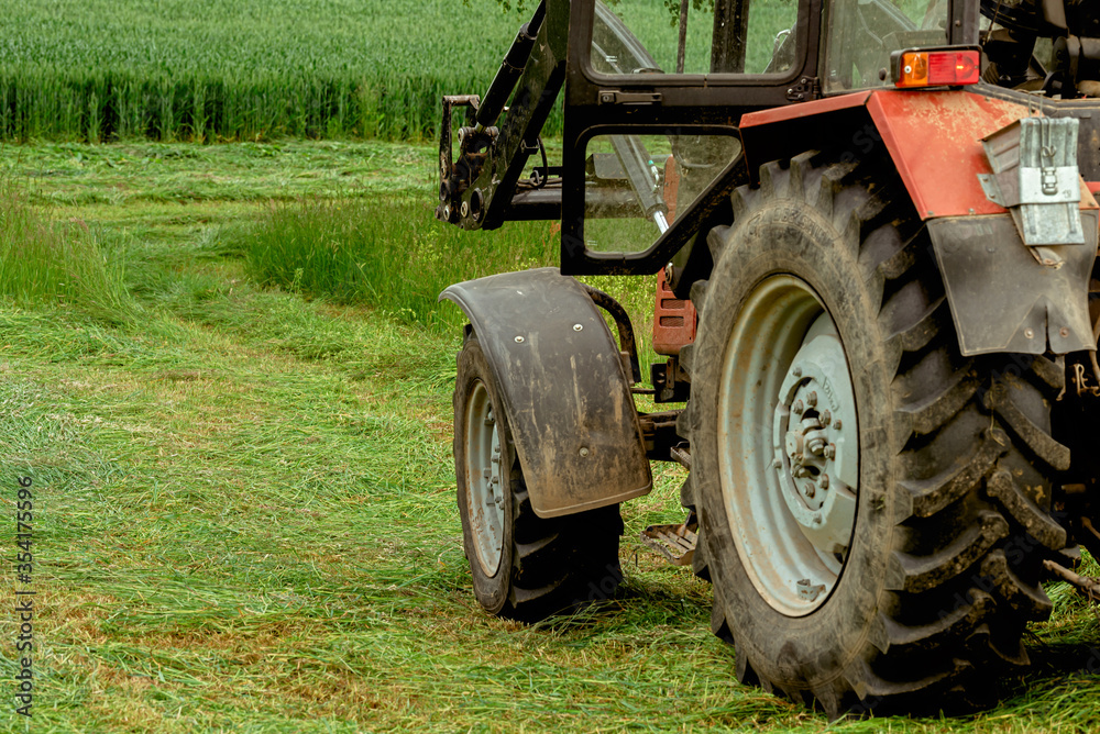 Obraz premium Tractor on a green meadow among mown grass