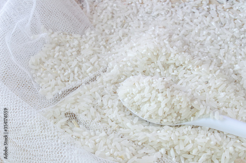 Raw white rice in spoon and bowl, on rice croton and winnowing tray background