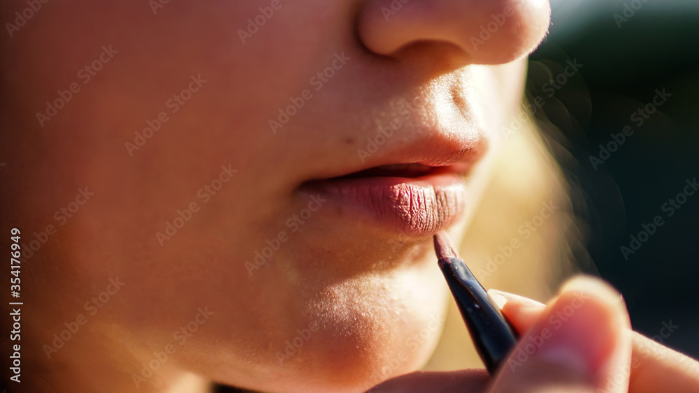 Young woman draw lips with red pencil.