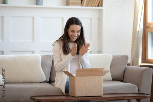 Excited young caucasian woman sit on sofa at home feel euphoric unbox internet order package, happy millennial female unpack box shopping online, satisfied with good quality product, delivery concept