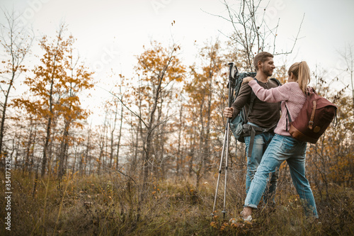 Couple of tourists in love stands embracing leaning on hiking sticks. Young Caucasian man and woman on the background of a young autumn forest. Support concept. © Svyatoslav Lypynskyy