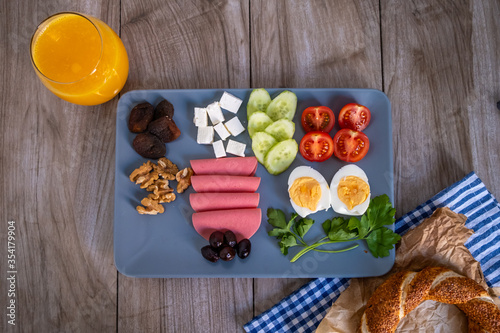 Top view of healty breakfast with orange juice,Turkish bagel, egg, tomato, chesee, walnut, cucumber, olive, salami and dried apricots  on gray plate