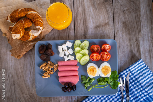 Top view of healty breakfast with orange juice,Turkish bagel, egg, tomato, chesee, walnut, cucumber, olive, salami and dried apricots  on gray plate