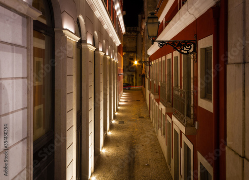 Narrow street with cobblestone pavement at night in Lisbon. Classic architecture buildings along empty alley in Portugal capital