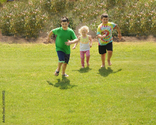 Three young children run on a grassy slope.