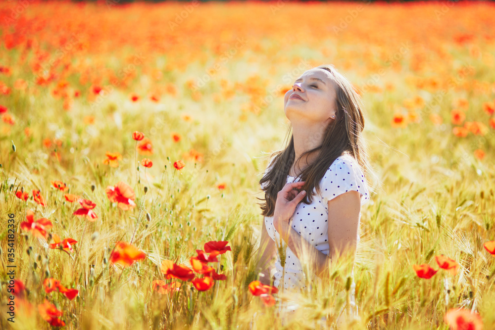 Beautiful young woman in white dress walking in poppy field on a summer day Beautiful young woman in white dress walking in poppy field on a summer day