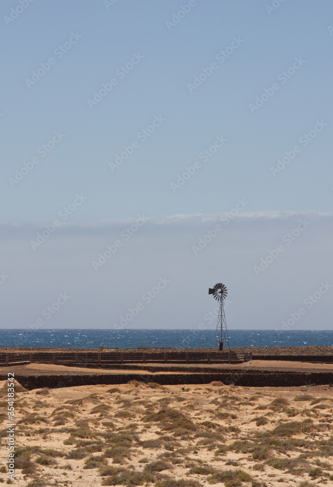 Wind pump near the old salt pans overlooking the cosat, Lobos Island Corralejo, Fuerteventura. Space left for copy text.