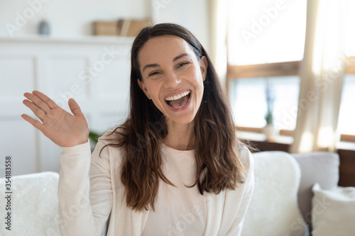 Headshot portrait of overjoyed young caucasian woman sit on couch at home wave greeting talking on video call, smiling millennial girl couch blogger say hello to subscribers, shoot live vlog on web