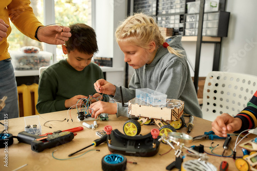 Quality and engineering. Young technicians building a robot, working with a wiring kit together with a male teacher at a stem robotics class. Inventions and creativity for kids