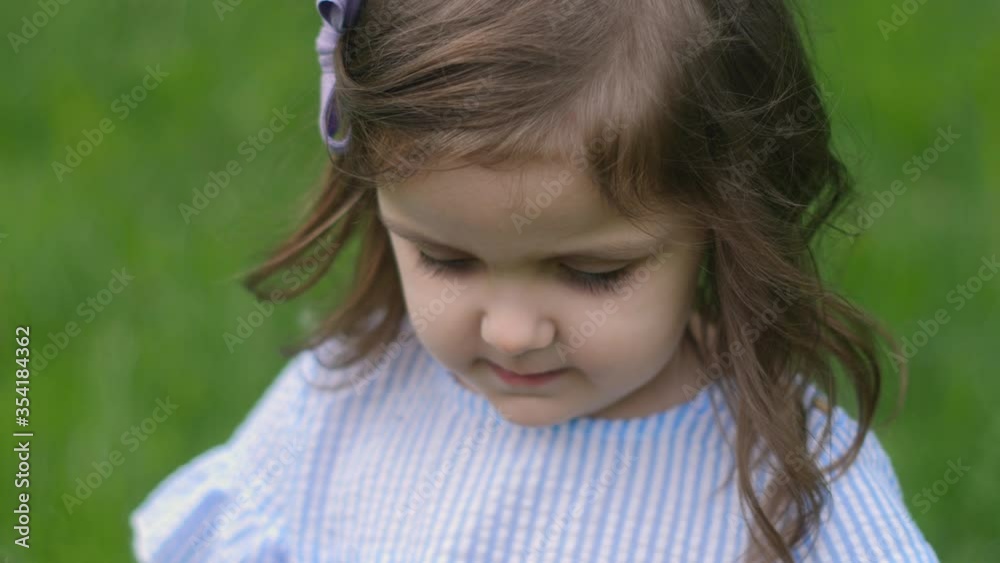 little beautiful girl in a blue dress stands in a green field with grass and holds a white dandelion in spring little beautiful girl in a blue dress stands in a green field with grass and holds a white dandelion in spring