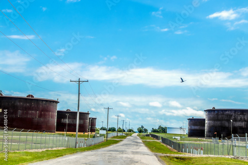 Road through tank farms with huge rusty petroleum tanks on either side and bird flying above in Cushing Oklahoma where most oil in USA is stored and traded