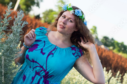Plus size girl in a blue dress and a wreath on her head is standing on the street.