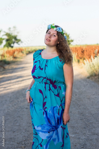 Plus size girl in a blue dress and a wreath on her head is standing on the street.
