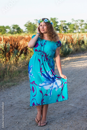 Plus size girl in a blue dress and a wreath on her head is standing on the street.
