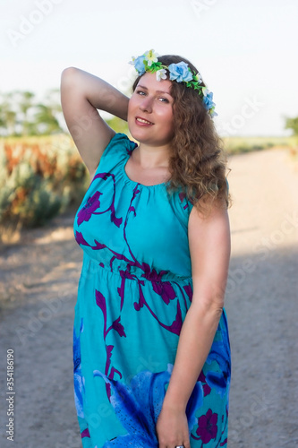 Plus size girl in a blue dress and a wreath on her head is standing on the street.