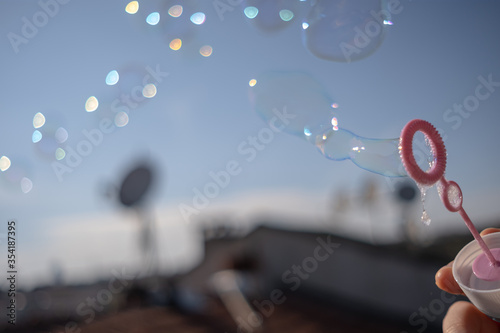 Young woman blowing soap bubbles. Side view of pretty auburn woman blowing soap bubbles on the roof