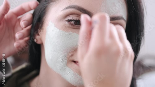 A pretty woman is doing beauty care procedure. Her friend is spplying a face mask on her face with a spatula. photo