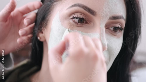 A pretty woman is doing beauty care procedure. Her friend is spplying a face mask on her face with a spatula. photo