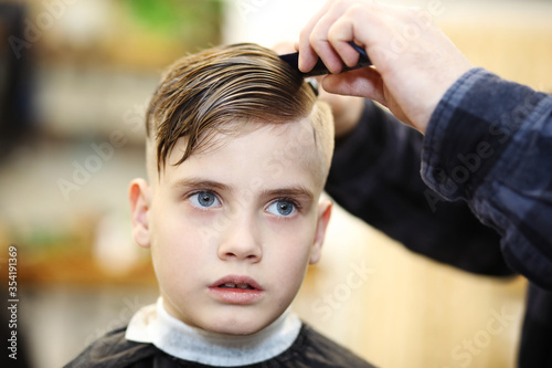 Hairdresser's hands making hairstyle to little boy, close up. Fashionable haircut for boys.