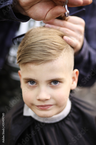 Hairdresser's hands making hairstyle to little boy, close up. Fashionable haircut for boys.