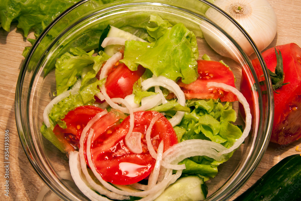 Vegetables salad in a glass bowl and vegetables lying on a wooden table Vegetables salad in a glass bowl and vegetables lying on a wooden table