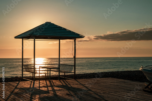 Empty summer cafe on the beach. No visitors due to pandemic and covid-19. Tables on a canopy, wooden flooring. Restaurant with sea view on the coastline. Closed borders, lack of tourists. Evening. Sun © Viktor