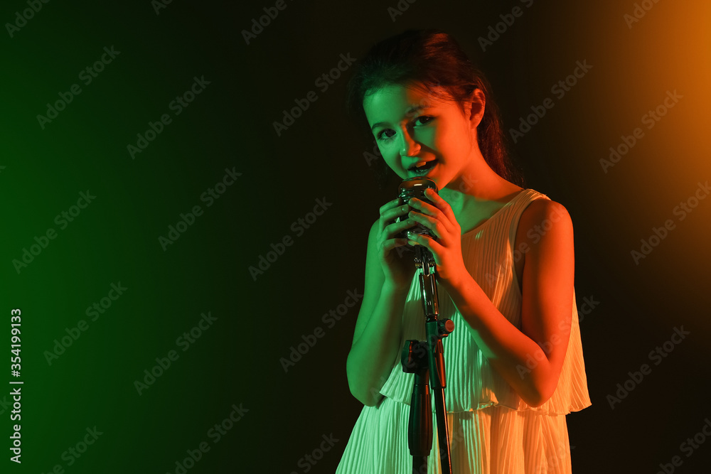 Obraz premium Cute little girl singing against dark background