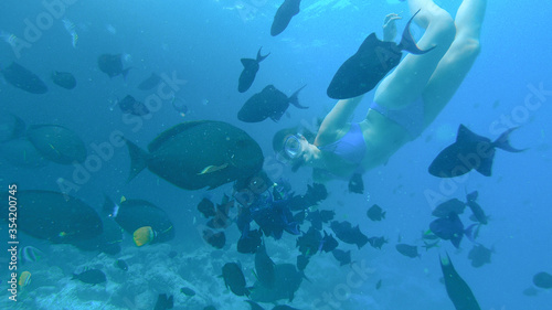 UNDERWATER: Young female tourist snorkeling around ocean feeds tropical fish