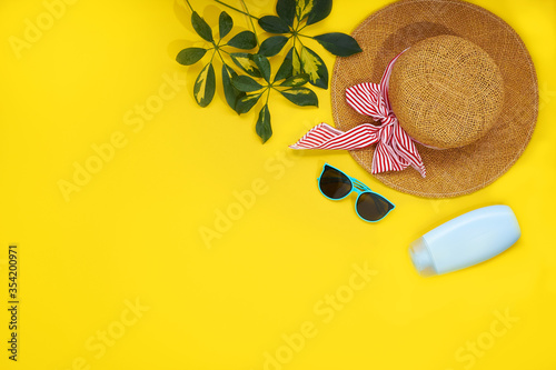 Accessories for the beach season. Straw hat, sunglasses, sunblock and leaves sheflers isolated on a yellow background. Top view flat lay photo