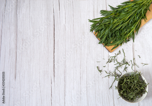 Drying of greens with preservation of vitamins. A bunch of fresh tarragon on a cutting board and a cup of dried tarragon on a light wooden background. Free space.