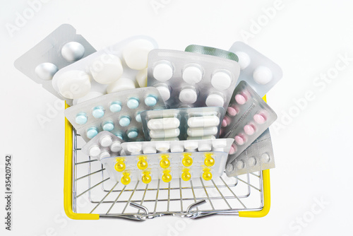 Various Pills in blisters are in a small shopping basket on a white background. Sale of drugs in stores and pharmacies. Health and medicine.