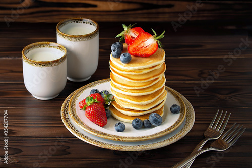 Close-up Homemade classic american pancakes with fresh blueberries, strawberries powdered sugar and two cups of milck.