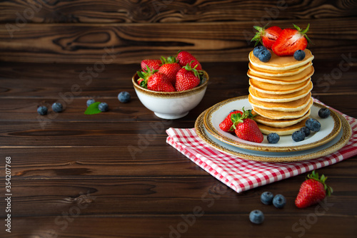 Testy homemade classic american pancakes with fresh blueberries and strawberries on wooden background.