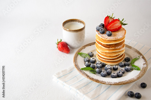 Cassic american pancakes with fresh blueberries, strawberries powdered sugar and milk. Healthy summer breakfast.