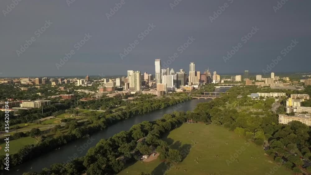 Aerial shot of people at park with skyscrapers against sky, drone flying backwards from green trees by river on sunny day - Austin, Texas Aerial shot of people at park with skyscrapers against sky, drone flying backwards from green trees by river on sunny day - Austin, Texas