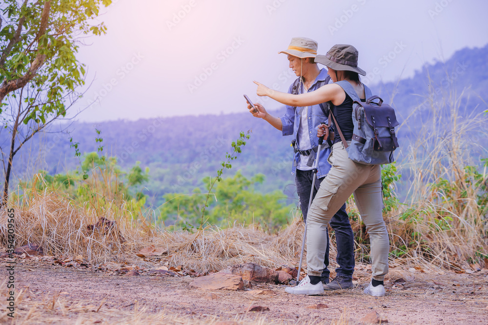 Couple hikers trekking at countryside dry forest using smartphone GPS on trail searching locations for their destination. Healthy lifestyle adventure hiking trip concept.